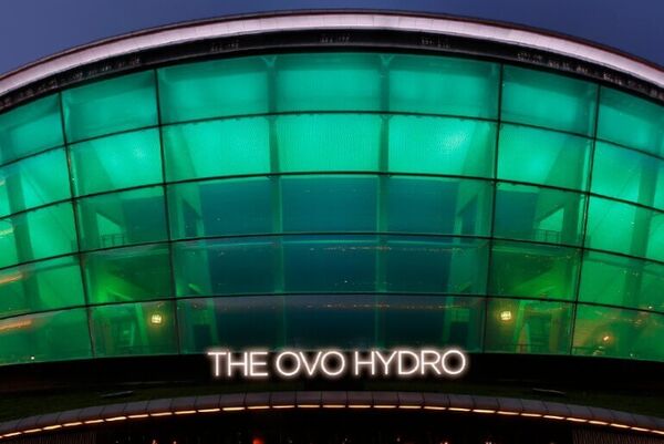A close-up of the entrance to the OVO Hydro which has a rounded roof and panelled frontage, which is all lit up green.