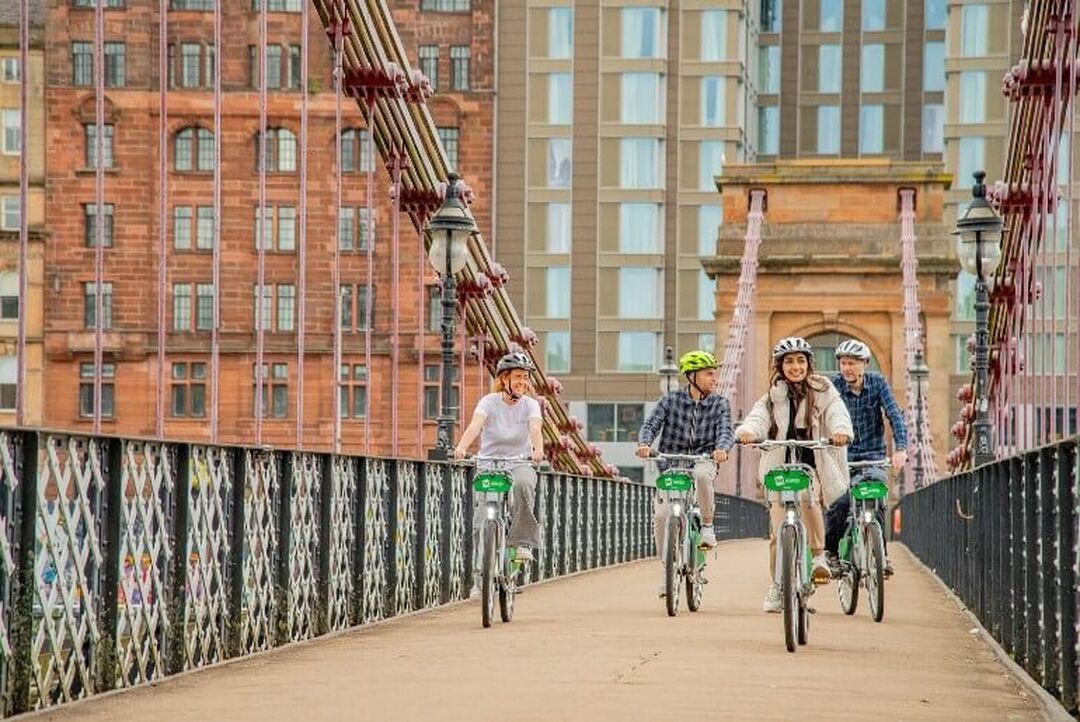 4 cyclists cycle across a bridge in the city centre.