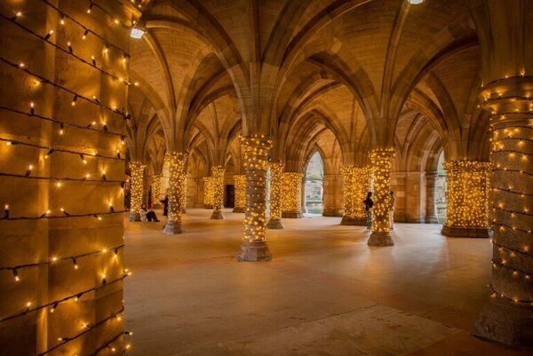 A series of old stone archways called Cloisters with fairy lights around the columns.