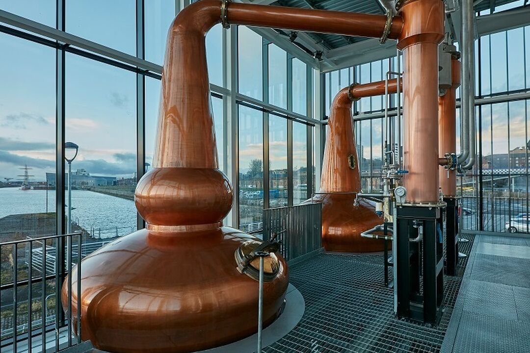 Two huge copper pots used for distilling sit by large windows overlooking the River Clyde.
