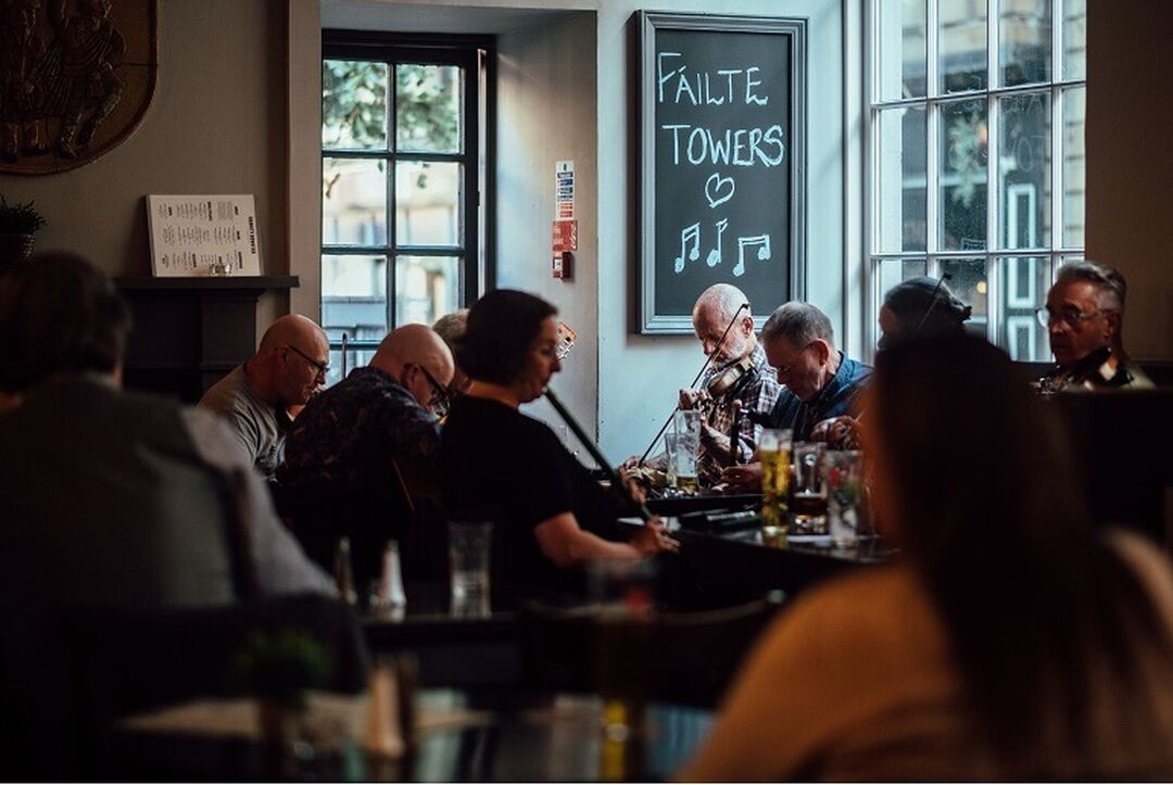 Musicians sit around a table in the corner of a bar playing a range of musical instruments.