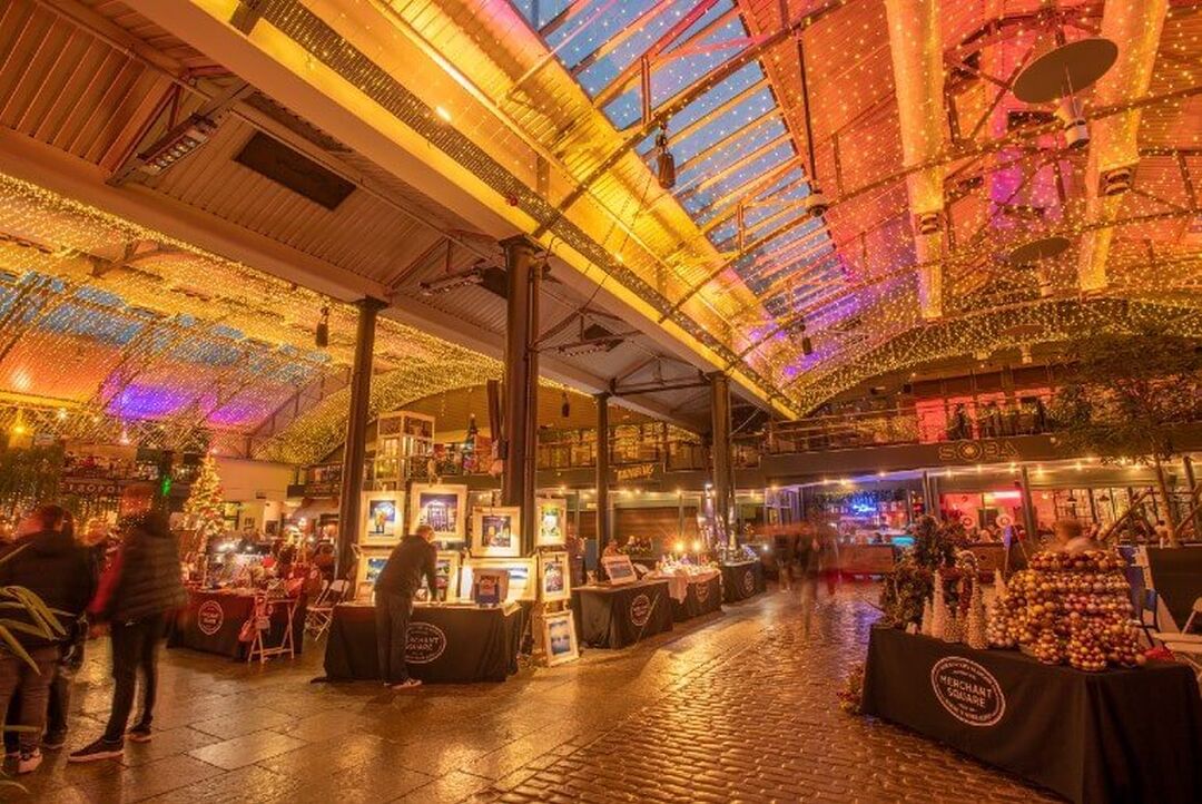 An indoor market with many stalls set up in a courtyard under a domed ceiling and fairy lights.
