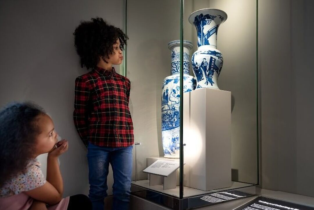 2 children look at a couple of vases behind a glass unit in a museum.