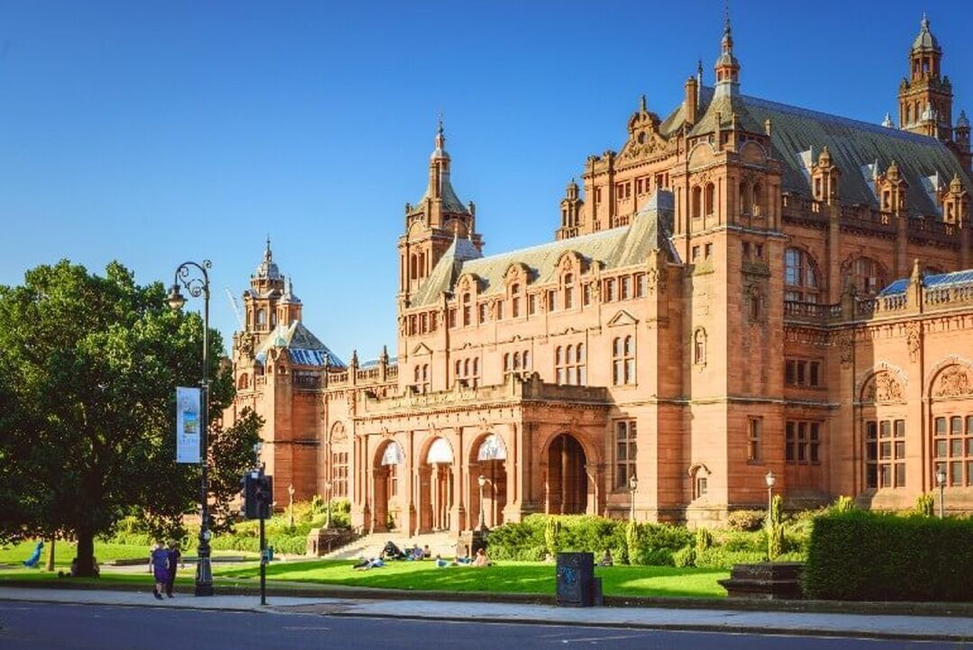 The exterior of Kelvingrove Art Gallery and Museum shows the Victorian brown sandstone building with its turrets rising into a blue sky.