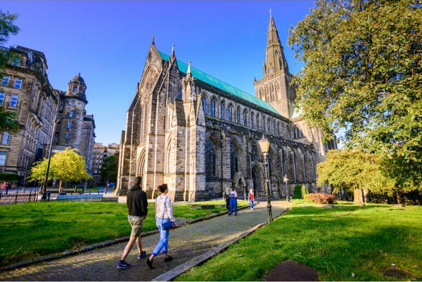A man and woman in the foreground walking along a path towards Glasgow Cathedral