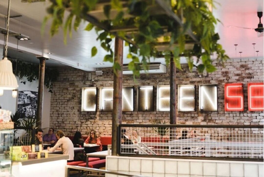 A neon lit up sign on an exposed brick wall says "Canteen 58" with diners sitting in the cool casual surrounds.