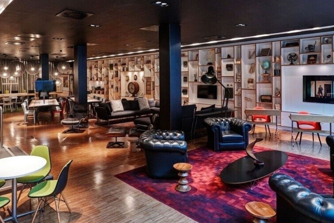 modern bar area with shiny floors, black leather couches, 50s retro tables and chairs, with black steel pillars down the centre of the room and a wall of shelves holding nic nacs