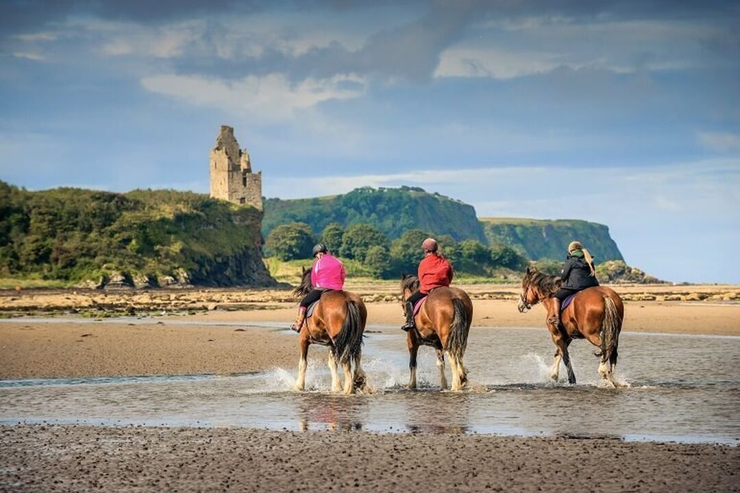 Three people riding Clydesdale horses on Ayr Beach.