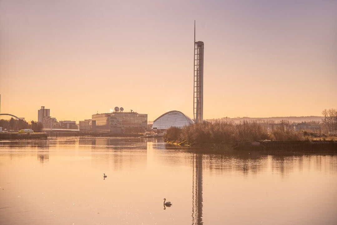 A pink-ish sky at sunset casts a warm glow across the River Clyde and modern Science Centre and tower.