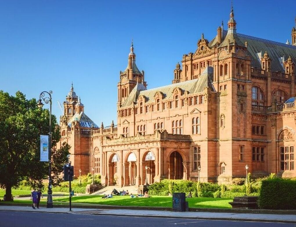The exterior of Kelvingrove Art Gallery and Museum shows the Victorian brown sandstone building with its turrets rising into a blue sky.